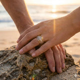Two hands with rings on a rock by the water at sunset