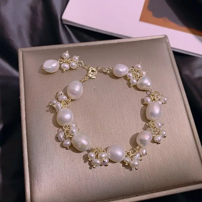 Gold-accented pearl charm bracelet laid out on textured surface, mermaid aesthetic.