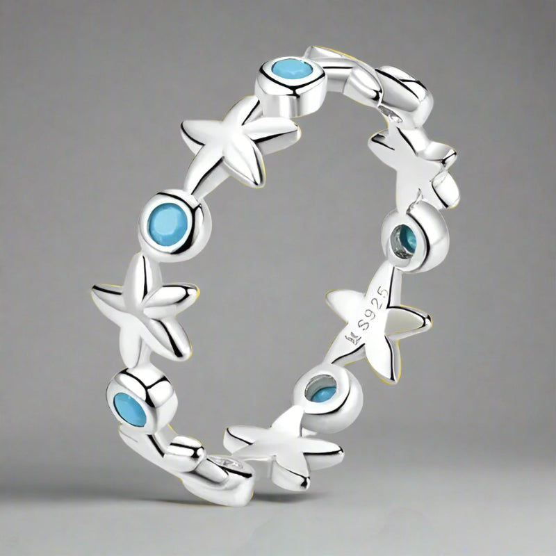 A sterling silver ring featuring a series of starfish shapes with blue zircon stones set in them, displayed against a neutral background.