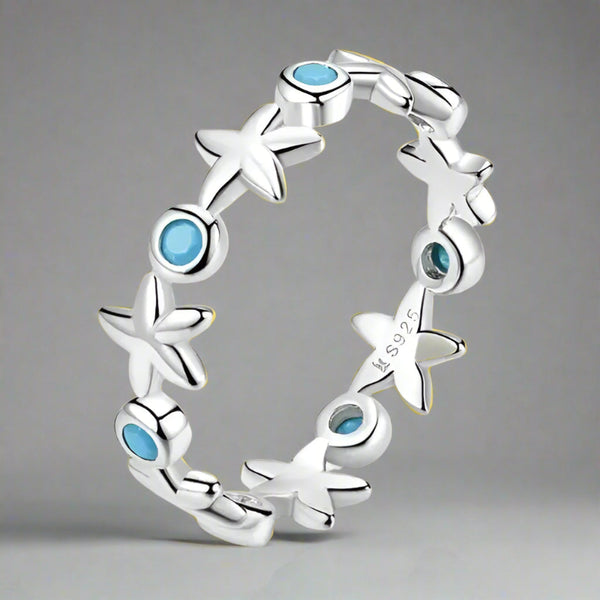 A sterling silver ring featuring a series of starfish shapes with blue zircon stones set in them, displayed against a neutral background.