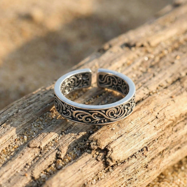Silver ring with intricate designs on a wooden surface