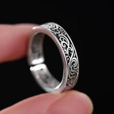 Silver ring with intricate design held between fingers against a black background