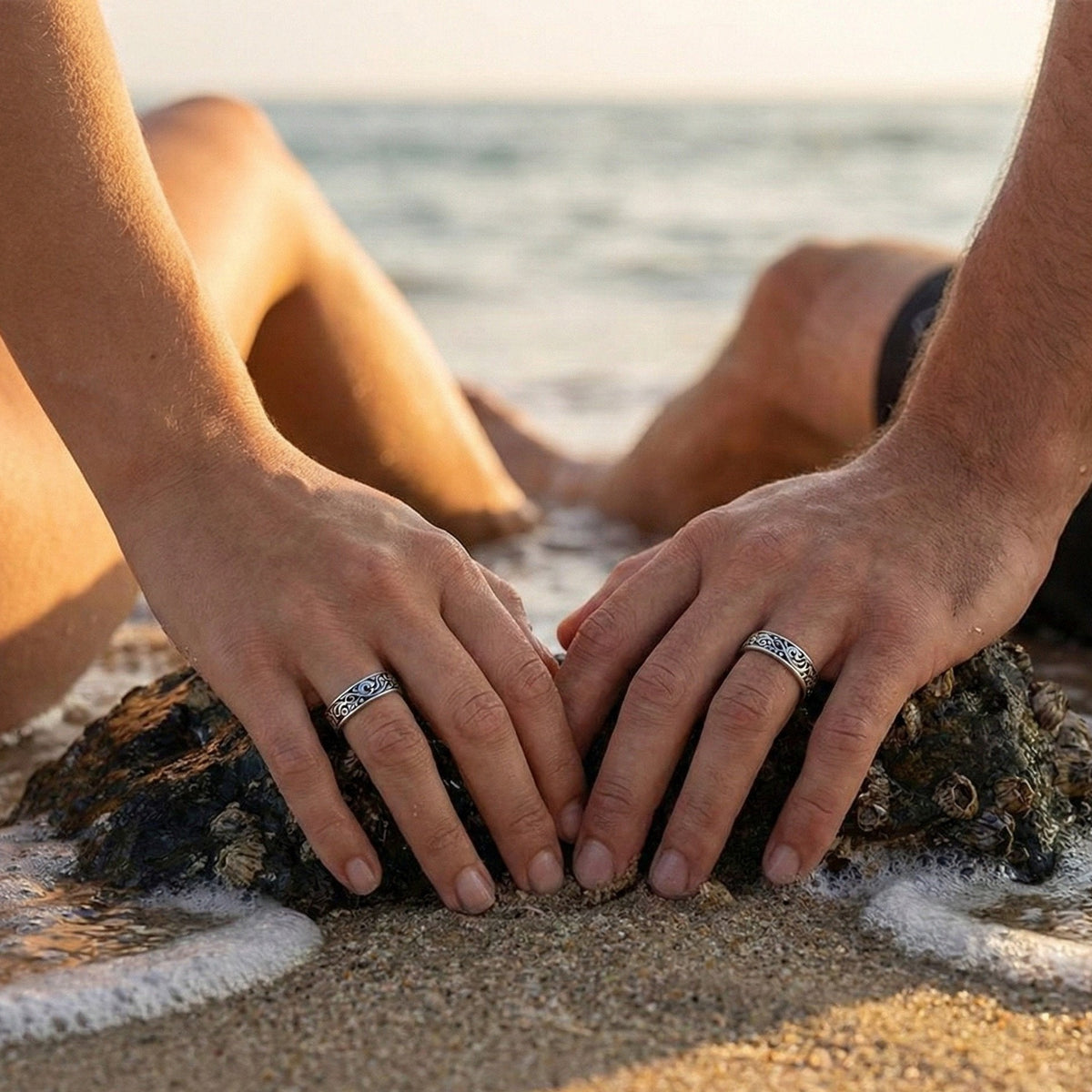 Two people's hands with rings on a rock by the water