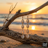 Cowrie shell dangle earrings on a branch with a sunset beach background