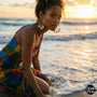 Woman in a colorful dress sitting by the ocean at sunset with Golden Cowrie Hoops