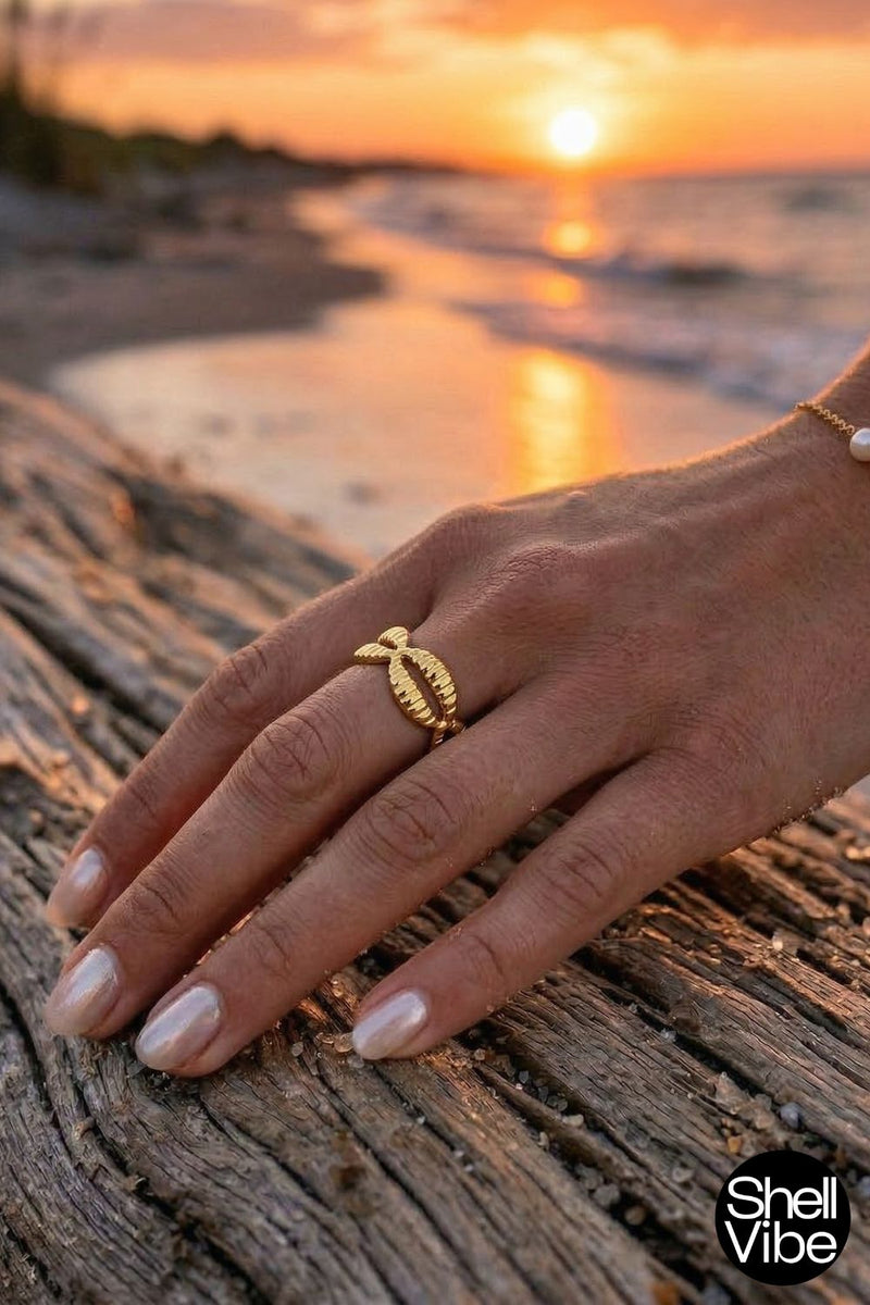 Hand wearing a gold cowrie ring  on a beach with sunset in the background