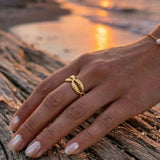 Hand wearing a gold cowrie ring  on a beach with sunset in the background