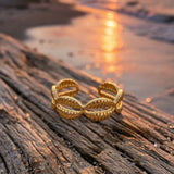 gold cowrie ring  on driftwood with a sunset over water in the background