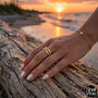 Hand wearing a gold cowrie ring on a beach with sunset in the background