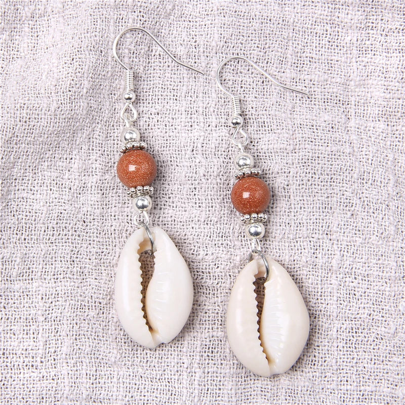 Pair of earrings with shell and bead design on a textured fabric background