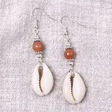 Pair of earrings with shell and bead design on a textured fabric background