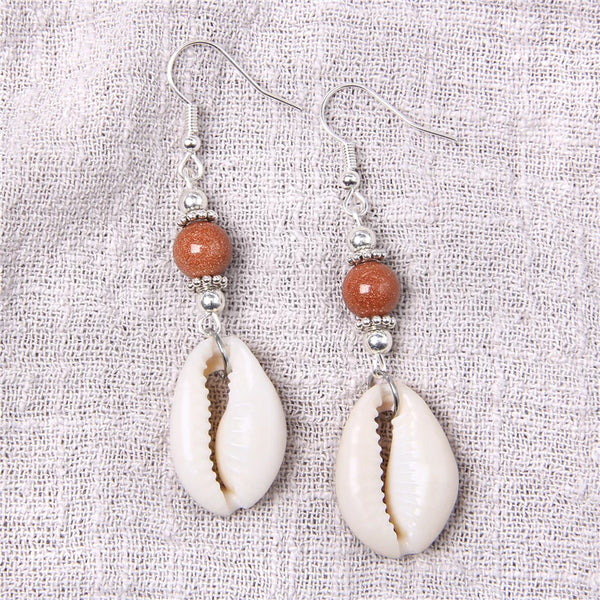 Pair of earrings with shell and bead design on a textured fabric background