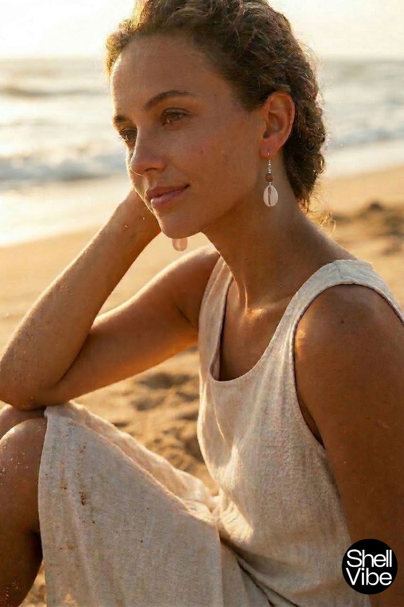 Woman sitting on a beach wearing cowrie earrings with a blurred background