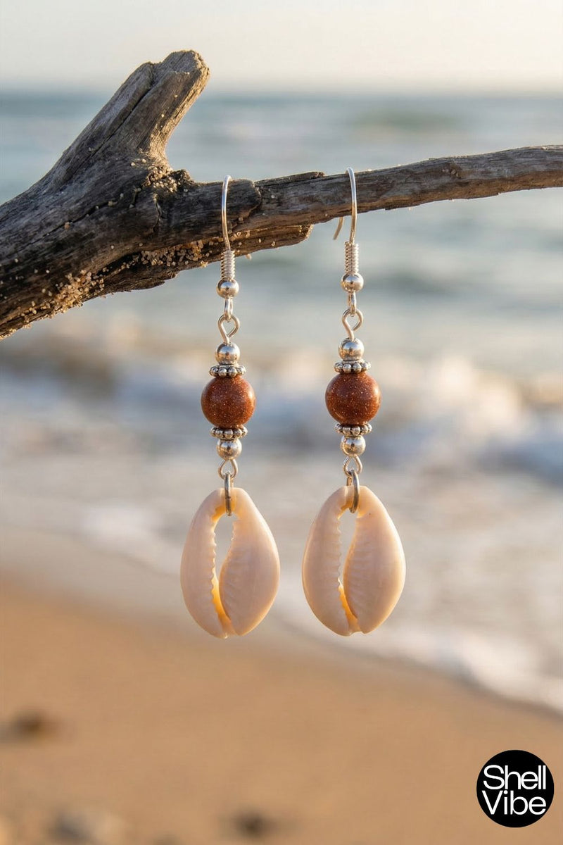 Cowrie shell earrings hanging from a branch with a beach background