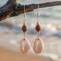 Cowrie shell earrings hanging from a branch with a beach background