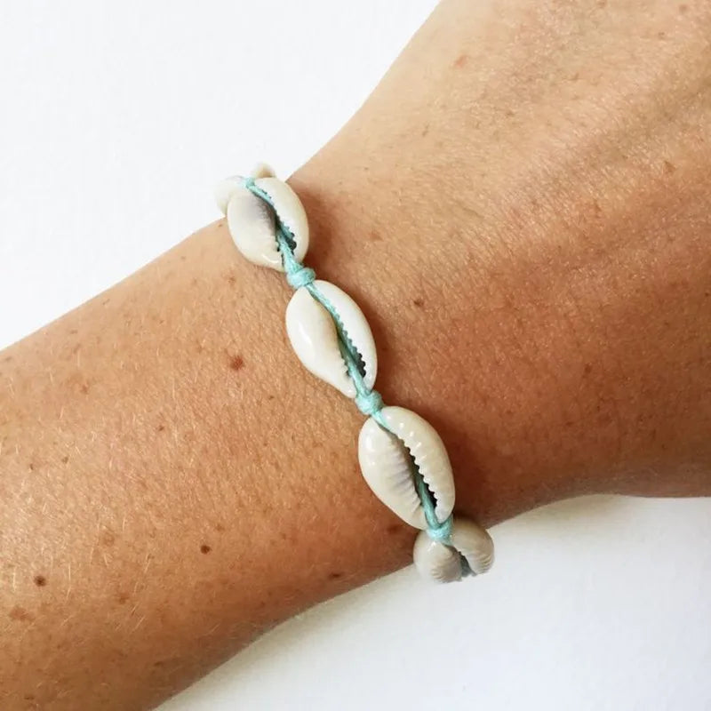 Bracelet with cowrie shell beads on a wrist against a white background