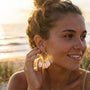 Woman wearing large cowrie hoop earrings with a blurred natural background