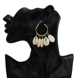 Gold hoop earrings with cowrie shells on a black mannequin ear.