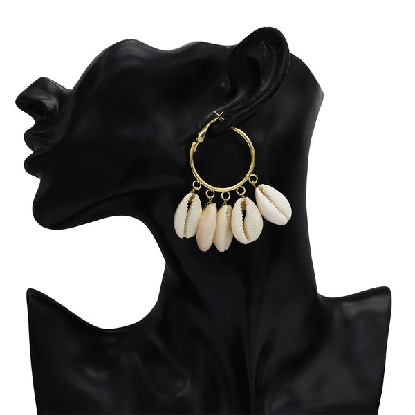 Gold hoop earrings with cowrie shells on a black mannequin ear.