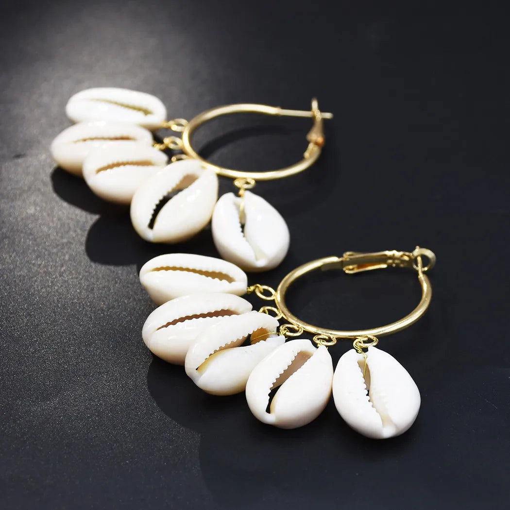 Pair of COWRIE HOOP earrings with gold hoops and white shell charms on a dark background