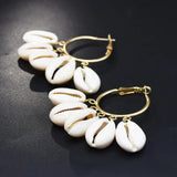 Pair of COWRIE HOOP earrings with gold hoops and white shell charms on a dark background