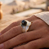 Hand wearing a sterling silver and gold pearl ring with a blurred beach background