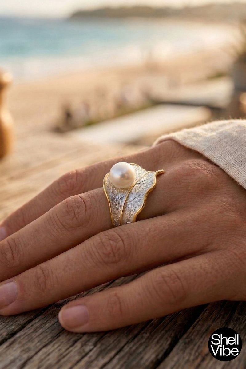Hand wearing a sterling silver and gold ring with a pearl on a wooden surface, blurred background