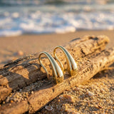 golden drop earrings  on a drift wood on sand.