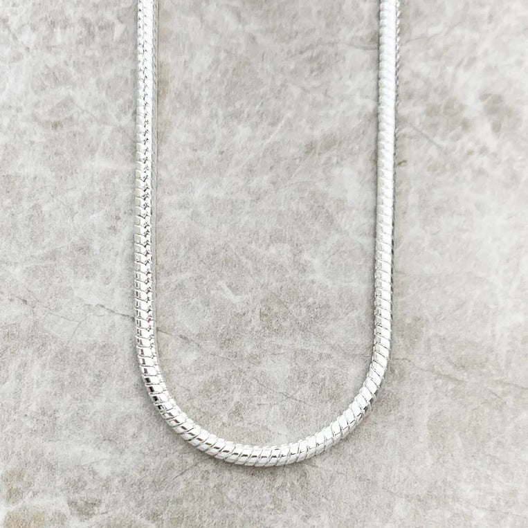 Sterling silver chain necklace on a textured gray surface with 'THADDAEUS' branding.