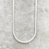Sterling silver chain necklace on a textured gray surface with 'THADDAEUS' branding.
