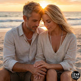 Couple sitting on a beach at sunset, holding hands with sterling silver necklaces