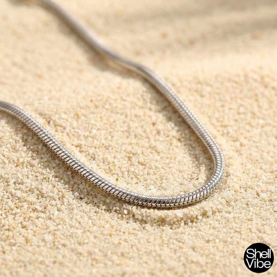 Sterling silver snake chain necklace on sand with 'Shell Vibe' brand logo.