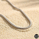 Sterling silver snake chain necklace on sand with 'Shell Vibe' brand logo.