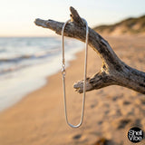Sterling silver necklace hanging from a branch on a beach with 'Shell Vibe' branding.