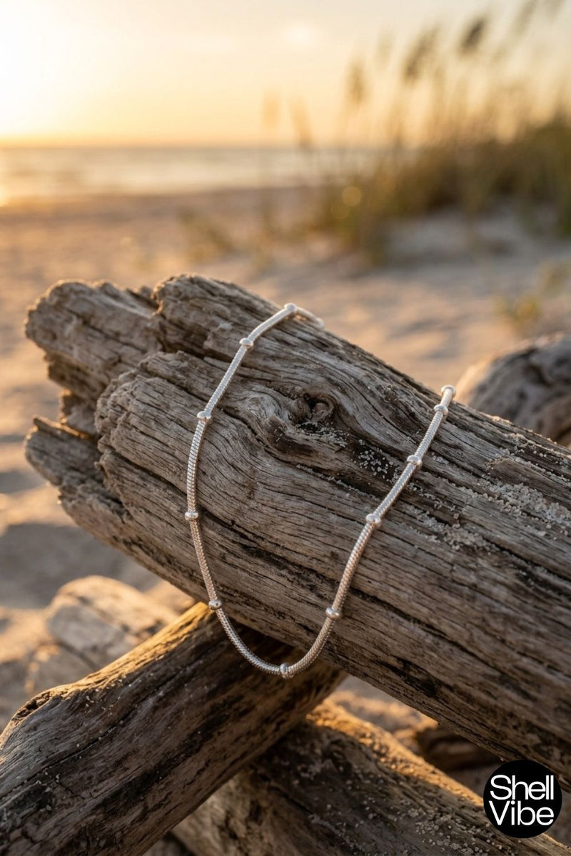 Driftwood with a necklace on a beach at sunset, featuring the brand 'Shell Vibe'.