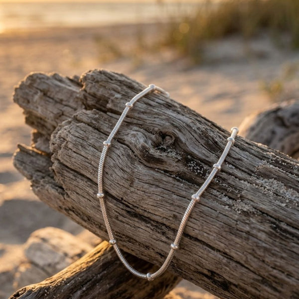 Driftwood with a necklace on a beach at sunset, featuring the brand 'Shell Vibe'.