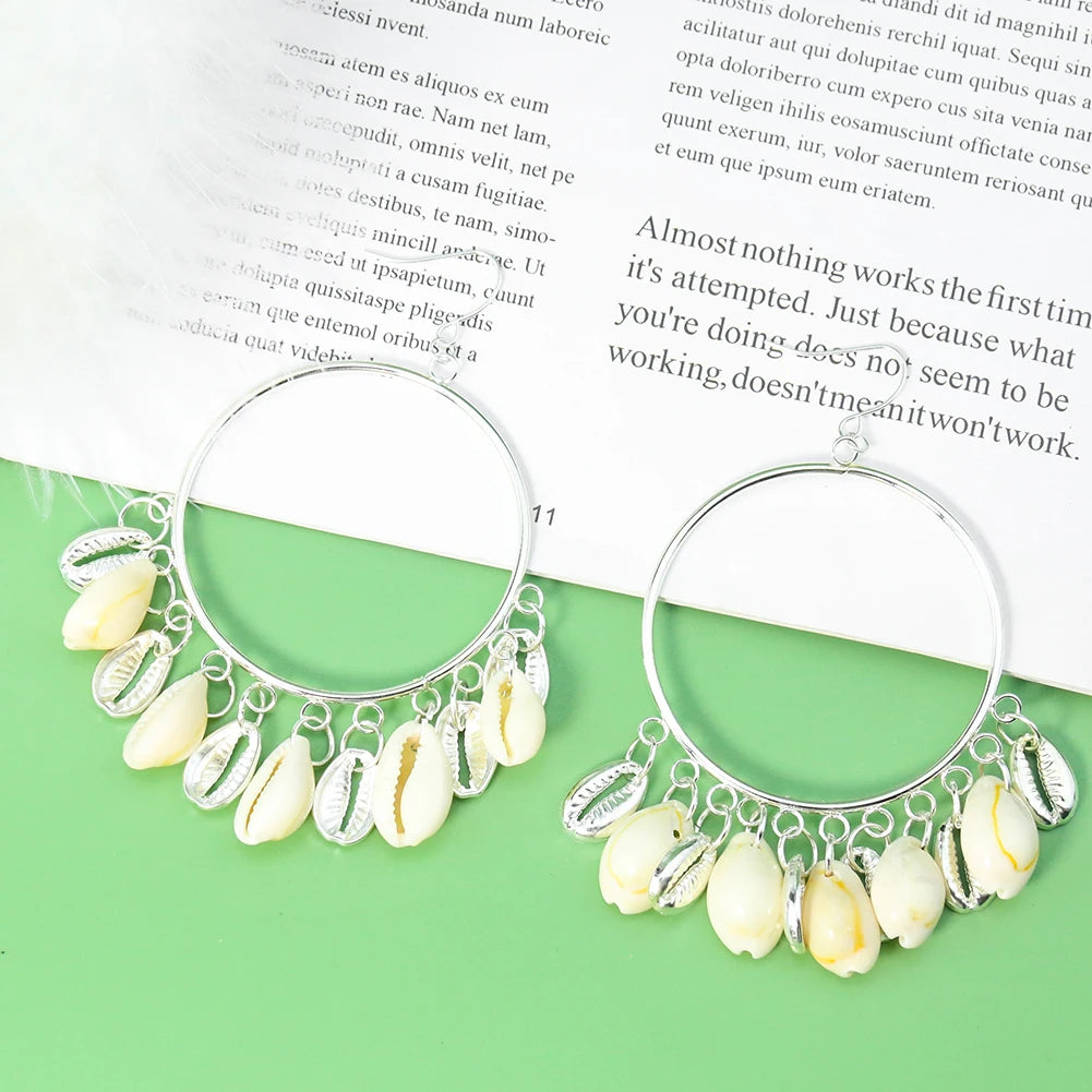 Silver hoop earrings with shell charms on a green surface