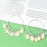Silver hoop earrings with shell charms on a green surface