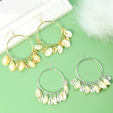 Gold and silver hoop earrings with shell charms on a green surface.