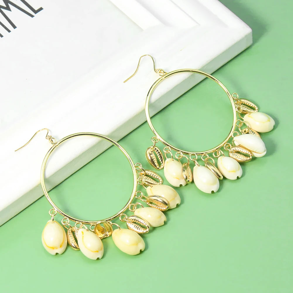 Gold hoop earrings with shell charms on a green surface