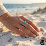 woman hand wearing a sterling silver turquoise ring on a sandy beach with 'Shellvibe' branding.