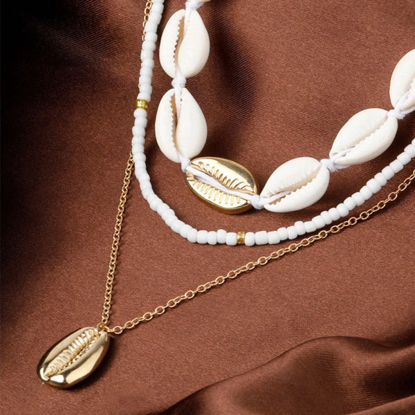 Necklace with white shell beads and gold chain on a brown fabric background