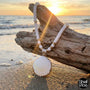Necklace with a shell pendant on a piece of driftwood on a beach at sunset.