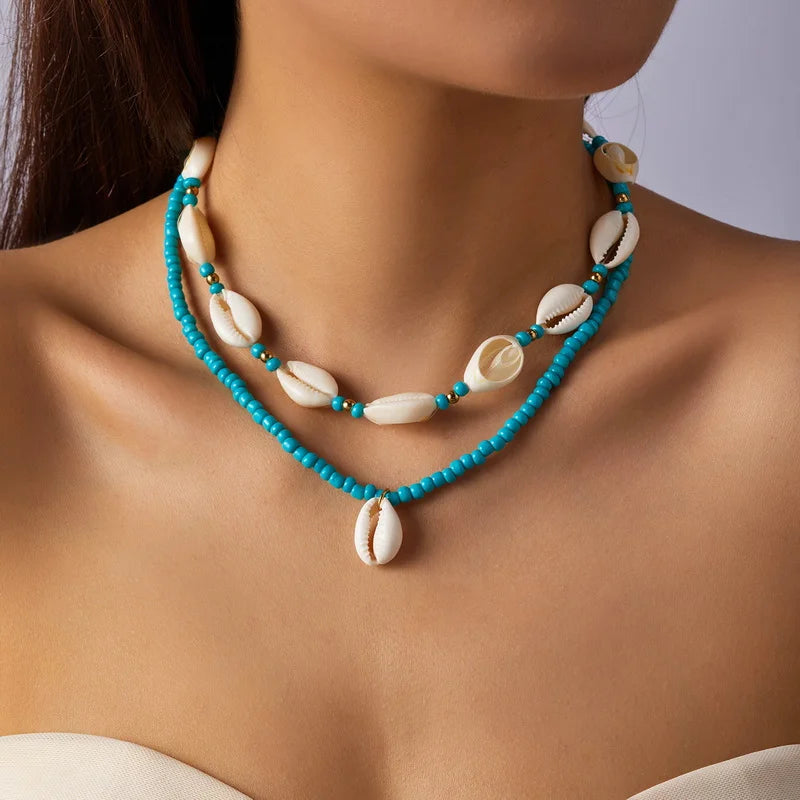 Necklace with turquoise beads and white cowrie shell pendants on a model against a neutral background