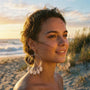 Woman wearing large cowrie hoop earrings on a beach at sunset