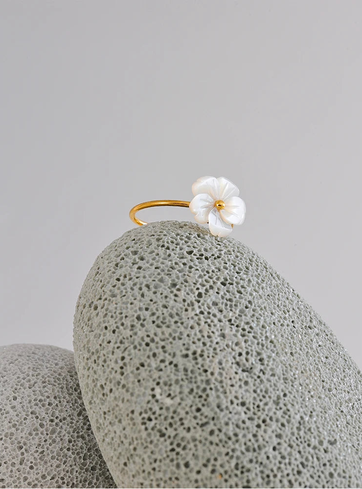 Gold ring with a white flower mother of pearl on a textured gray coral surface