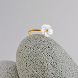 Gold ring with a white flower mother of pearl on a textured gray coral surface