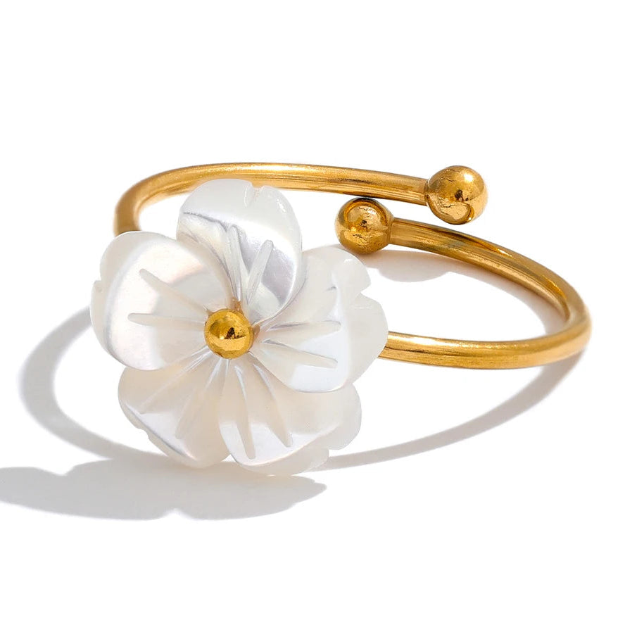 Gold ring with white floral mother of pearl design on a white background.