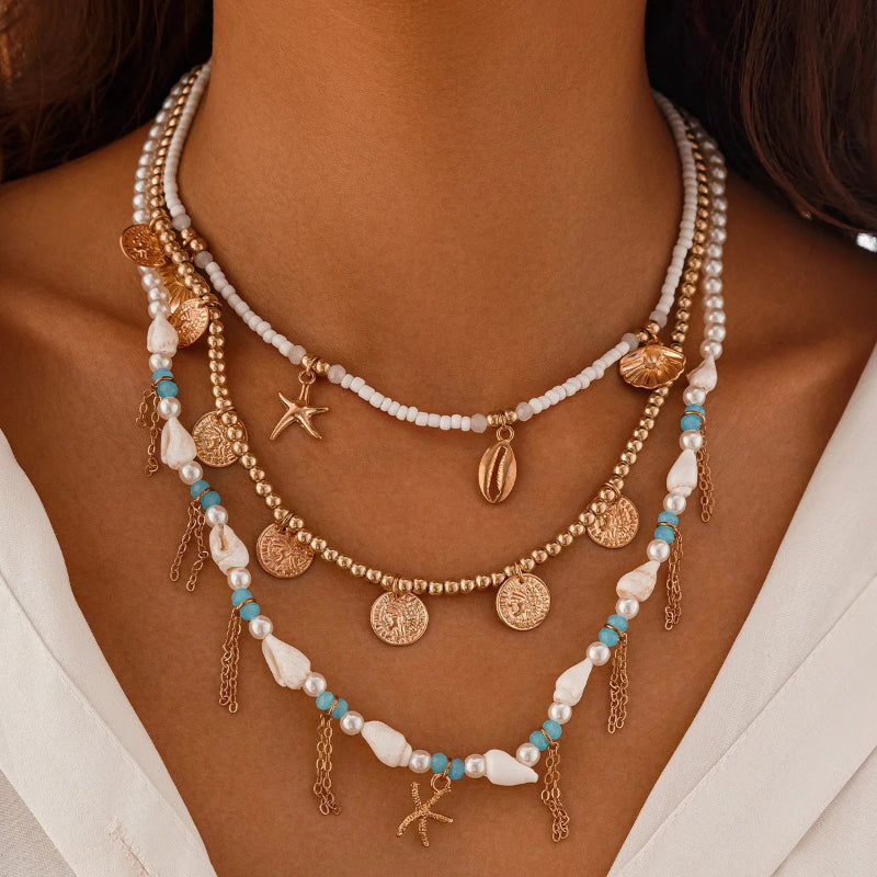 Necklace with pearls, coins, and starfish charms, beaded cowrie and scalope shells on a woman wearing a white top.