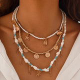 Necklace with pearls, coins, and starfish charms, beaded cowrie and scalope shells on a woman wearing a white top.